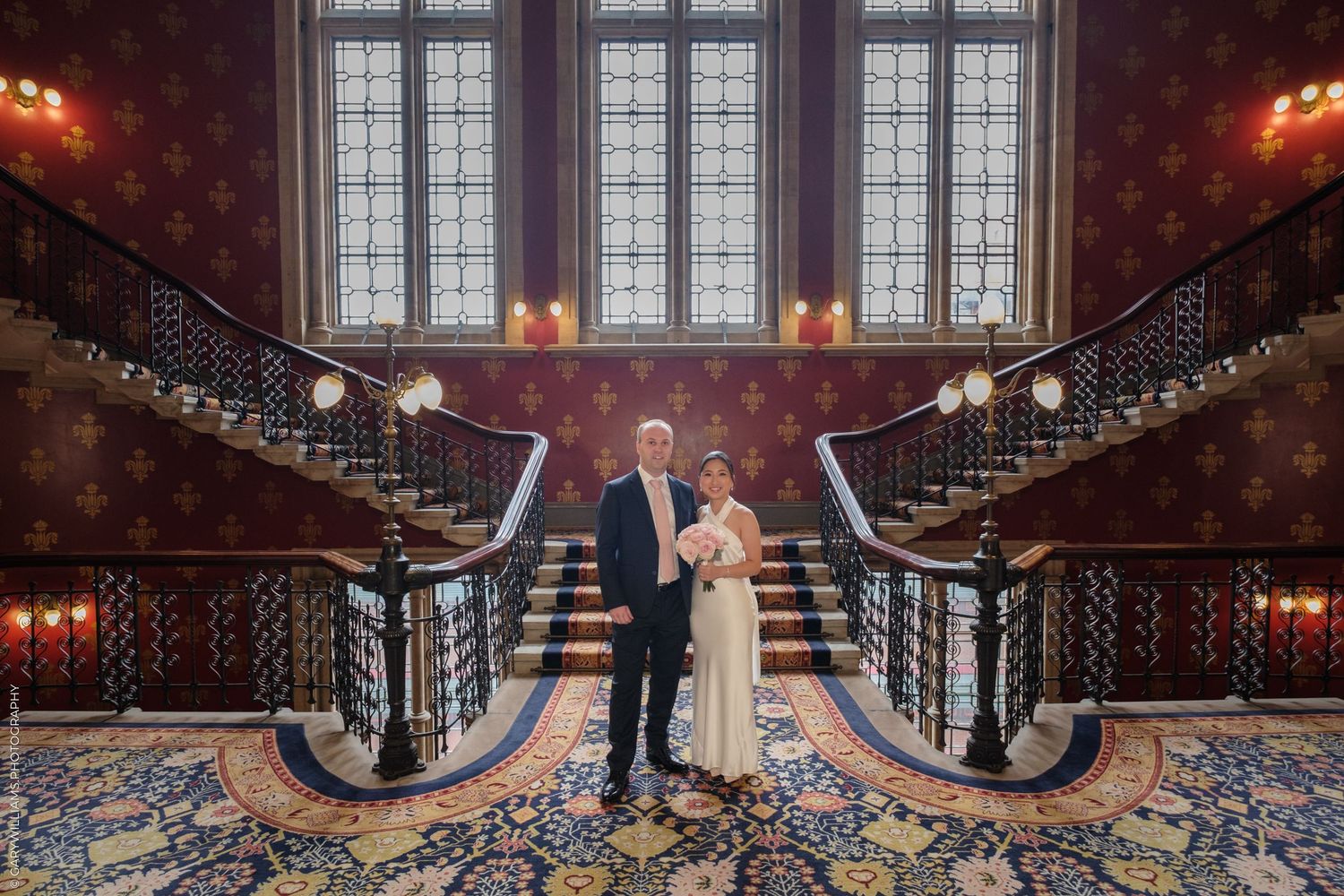 A grand spiral staircase with ornate wrought iron railing inside an elegant mansion with classical decor and lighting.