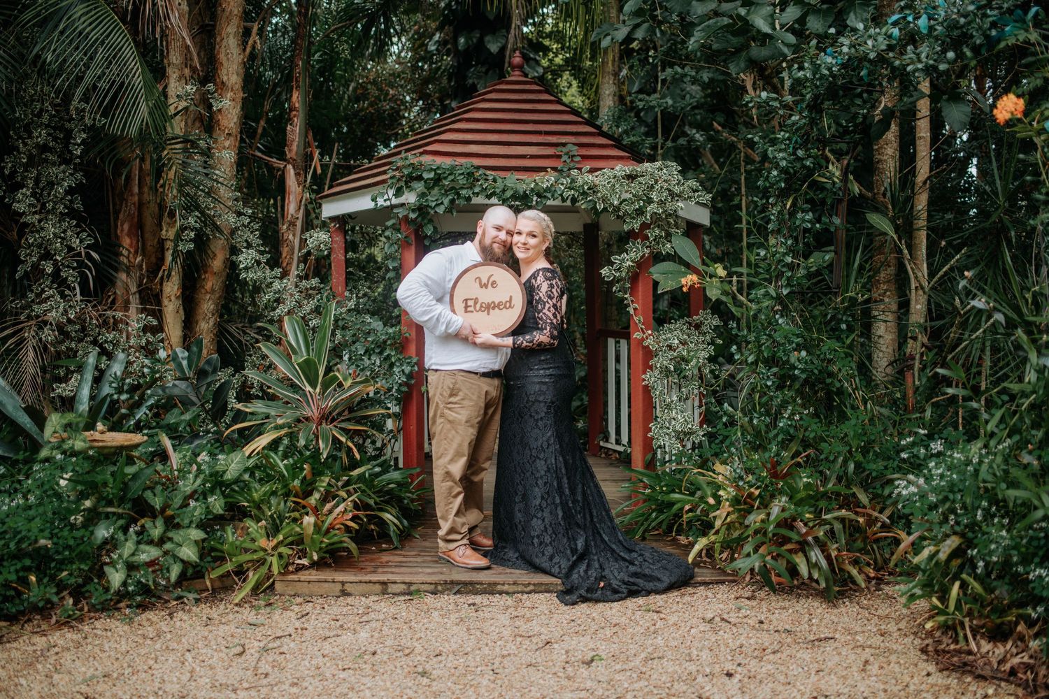 Two people embrace during their first dance as spouses at an outdoor wedding celebration with lush greenery backdrop.