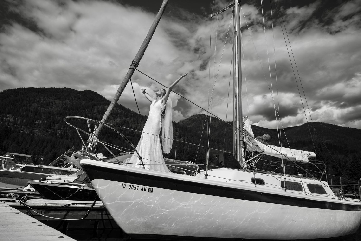 A dramatic black and white photo series showing sailboats moored in a harbor against cloudy skies and mountainous backdrops.