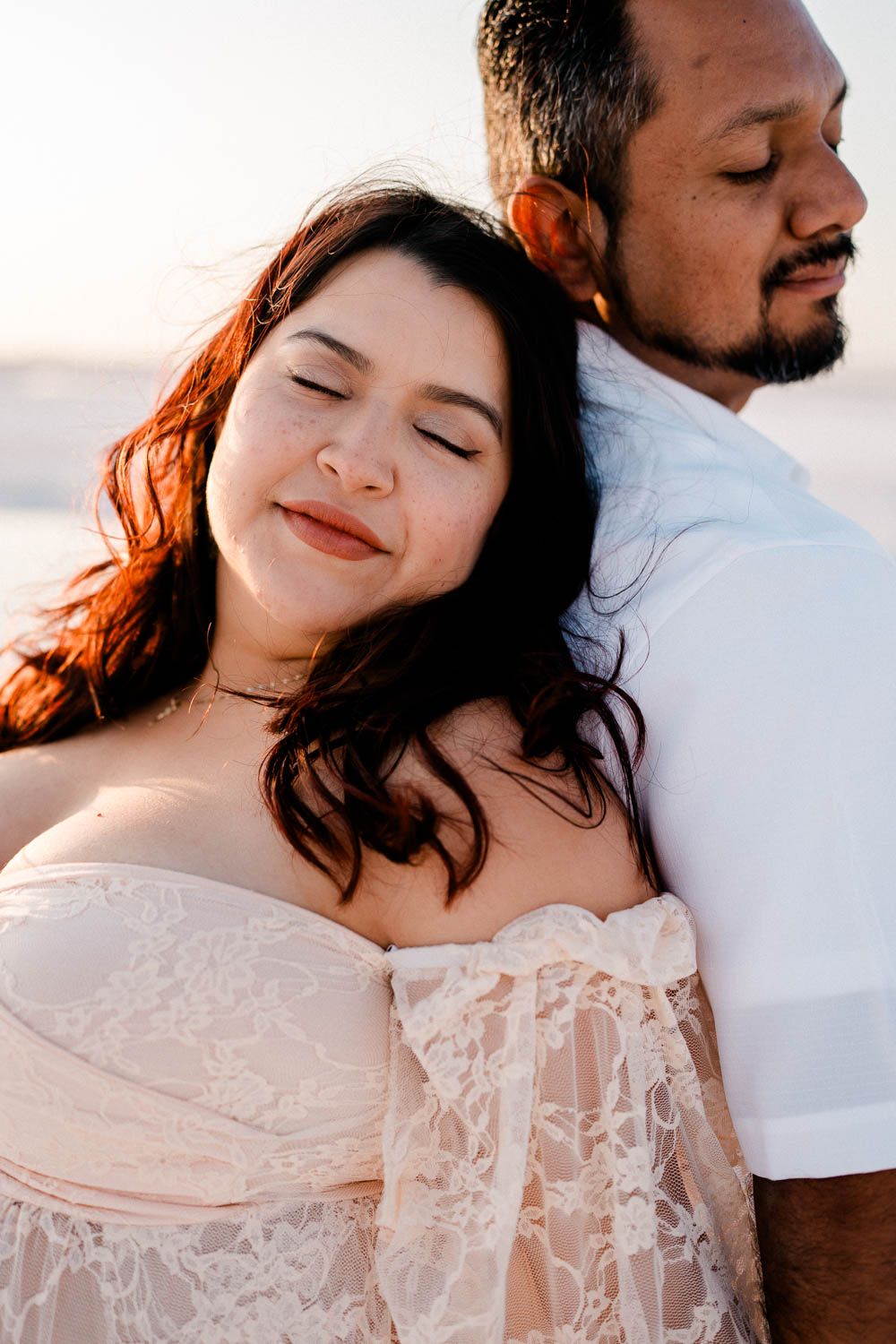 A romantic beach photoshoot shows a couple in intimate poses with white lace dress against sunset lighting.