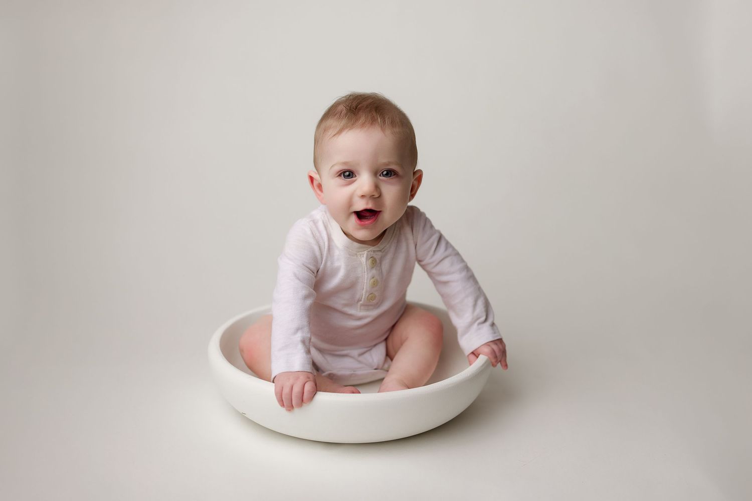 Baby wearing white clothing appears to grow throughout five consecutive milestone photos showing development stages.