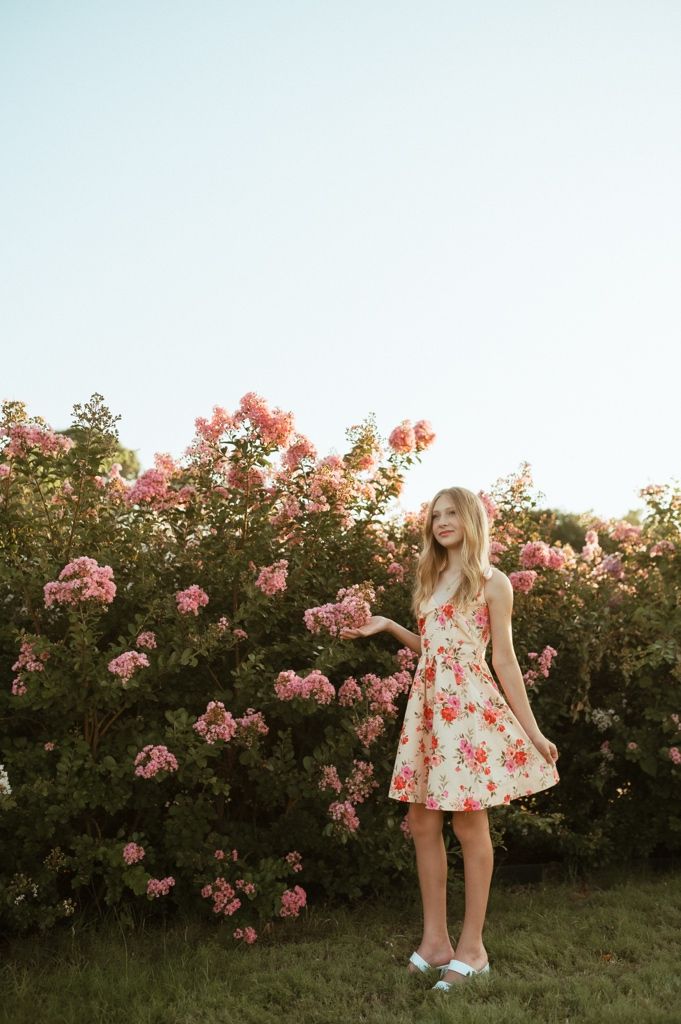 A floral sundress complements the blooming pink roses in a garden at sunset.