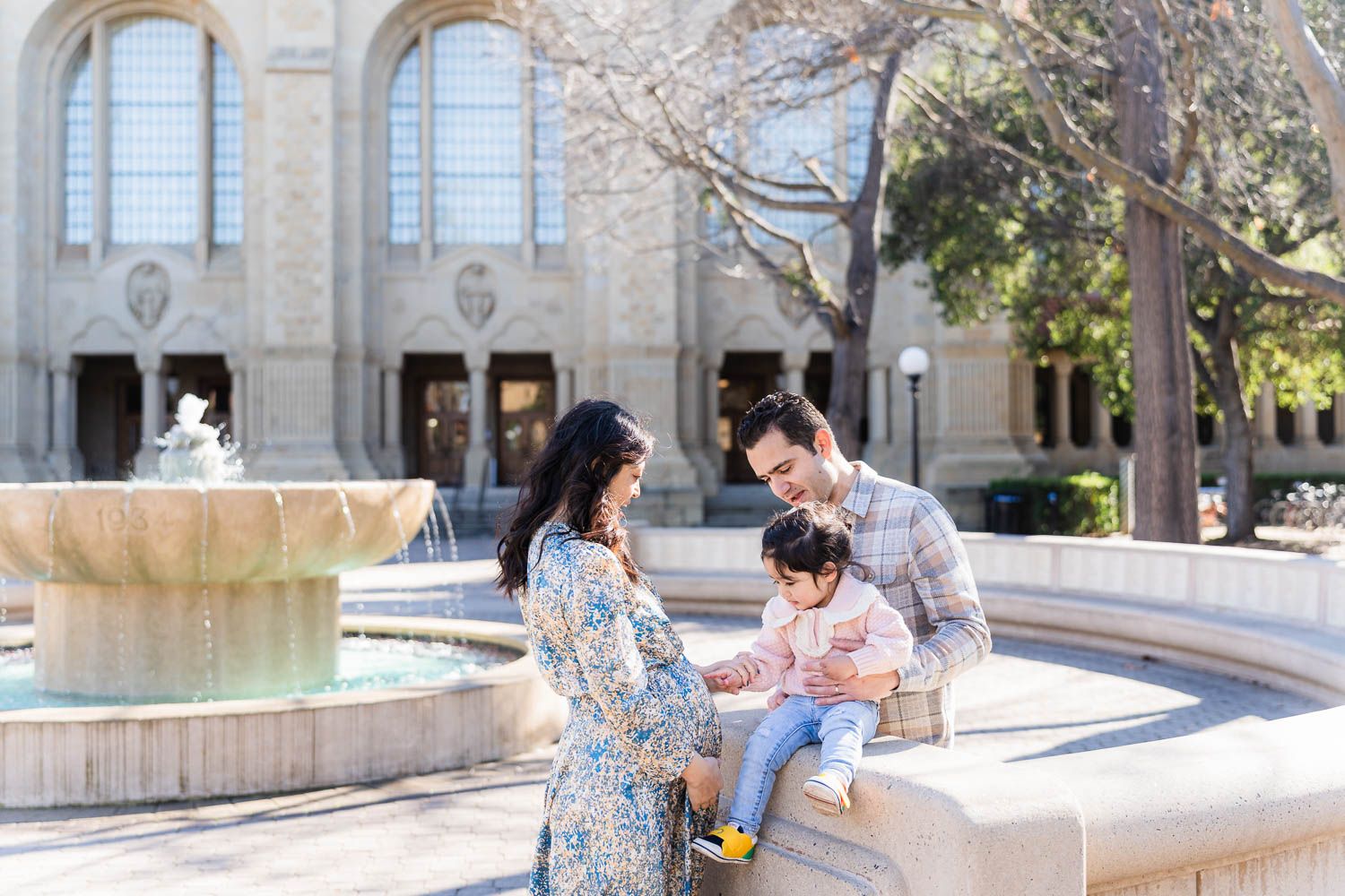 People enjoying a sunny day at the campus courtyard with stone architecture and benches in the background.