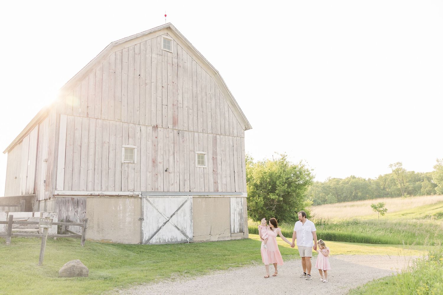 A white rustic barn with gambrel roof stands in a pastoral setting on a sunny summer day.