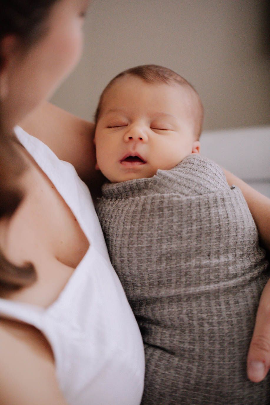 A peaceful sleeping baby nestled in soft gray knit clothing and white blanket captured in a tender closeup series.