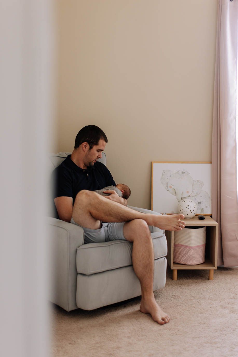 A person relaxes on a gray armchair in a minimalist room with pink decor accents and artwork.