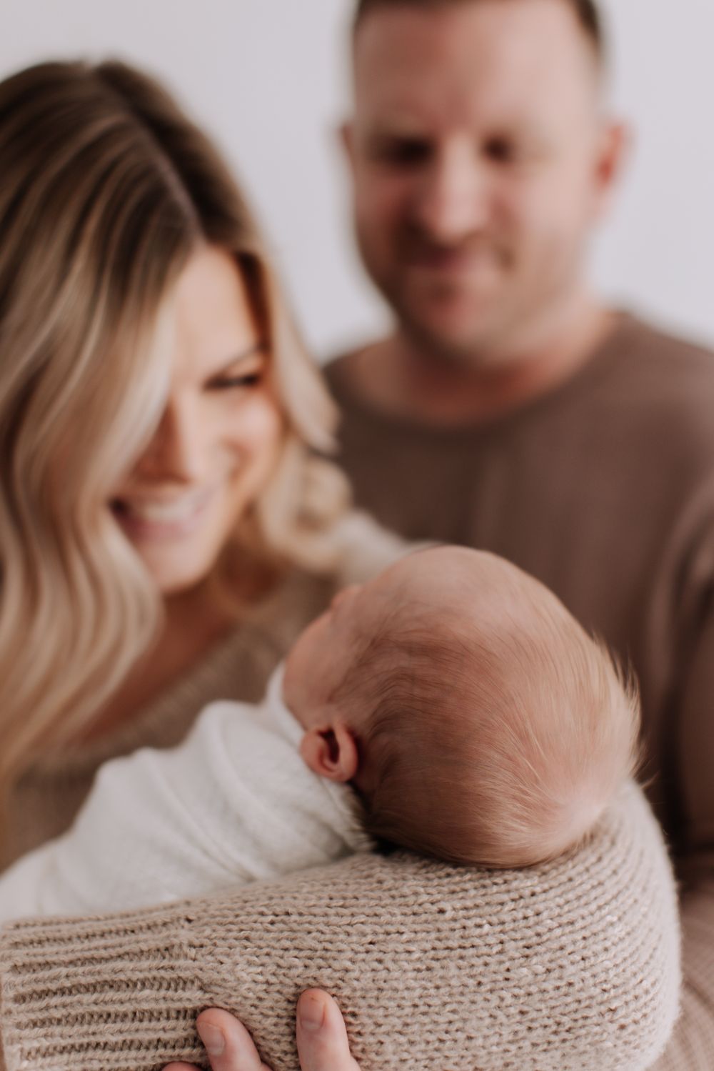 A cozy intimate portrait series showing tender family moments with a swaddled newborn in beige knit blanket.