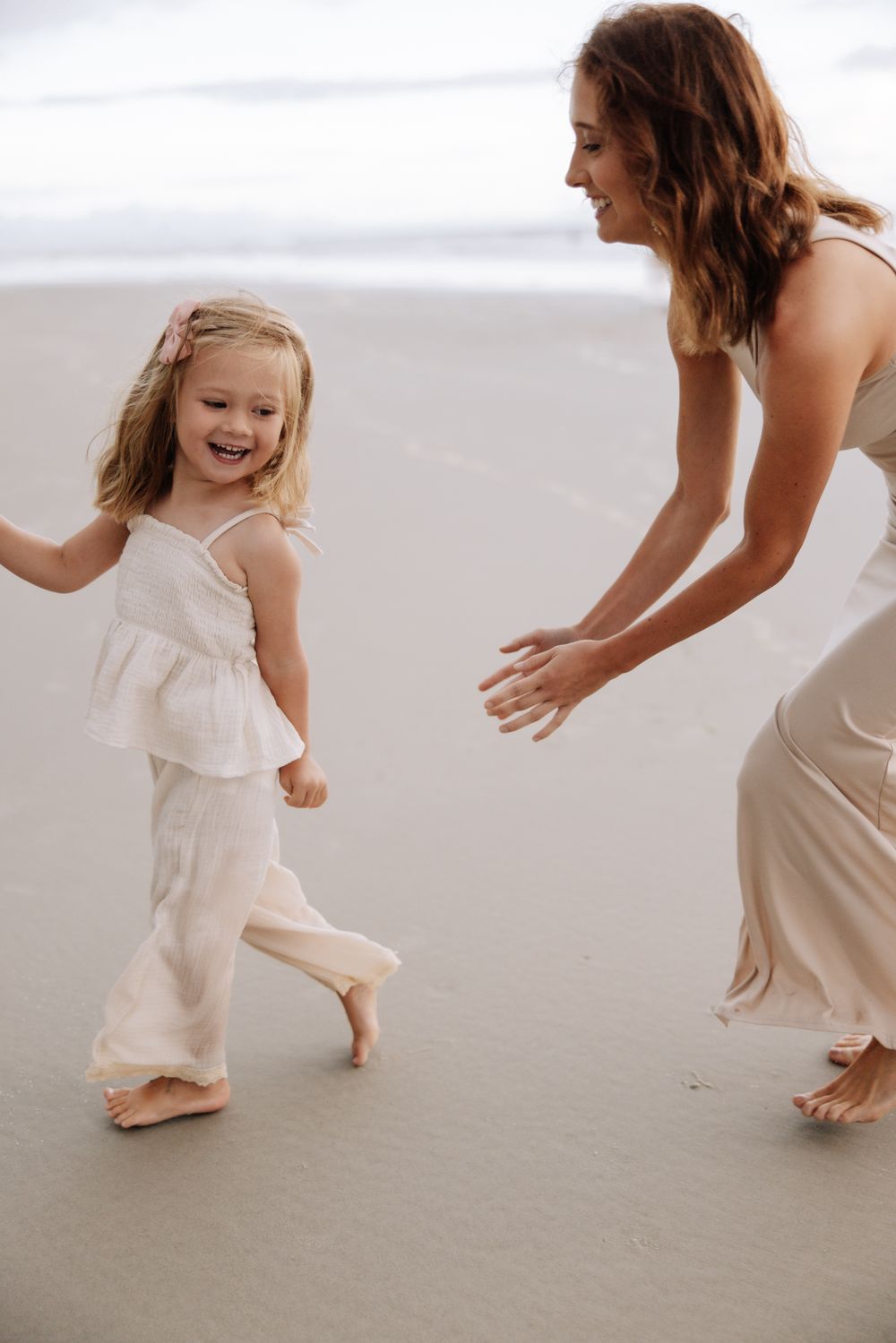 A joyful moment between two people dancing together on a peaceful beach while wearing flowing white and beige dresses.