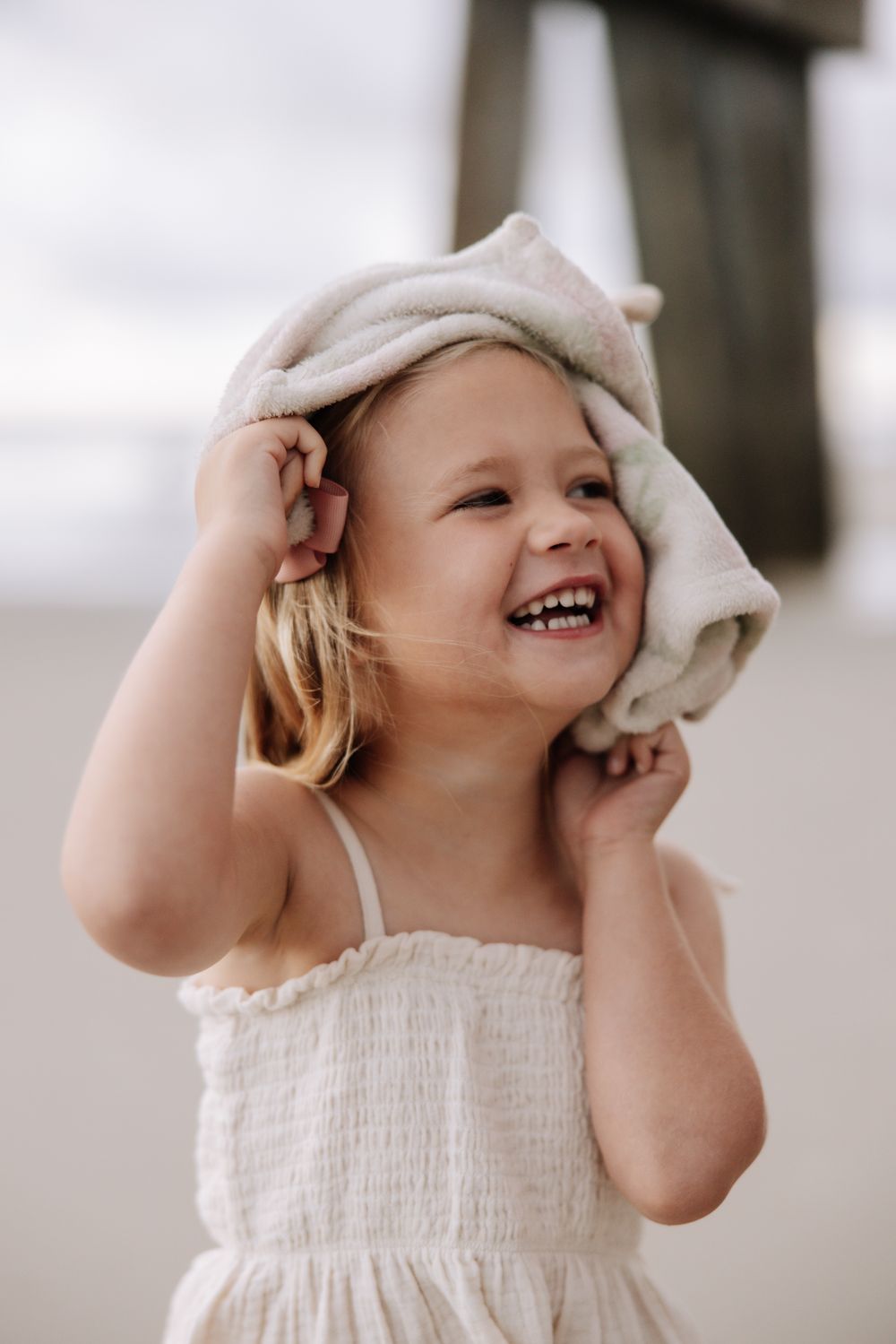 A joyful young child in a white dress smiles while wrapping a towel around their head.