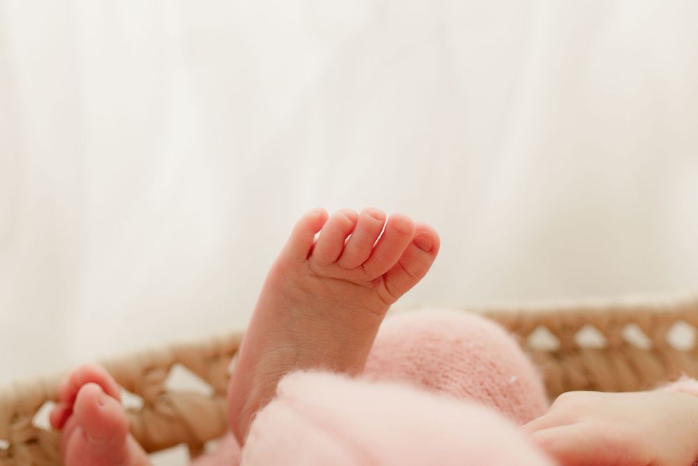 Close-up of tiny newborn baby foot against soft pink blanket in woven basket.