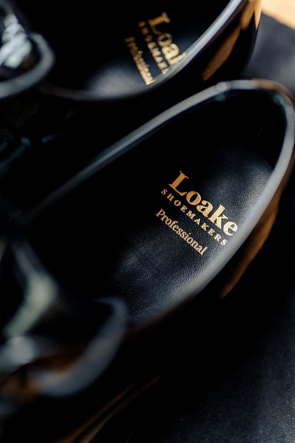 Close-up shot of black leather shoes with gold Loake branding in elegant lighting.
