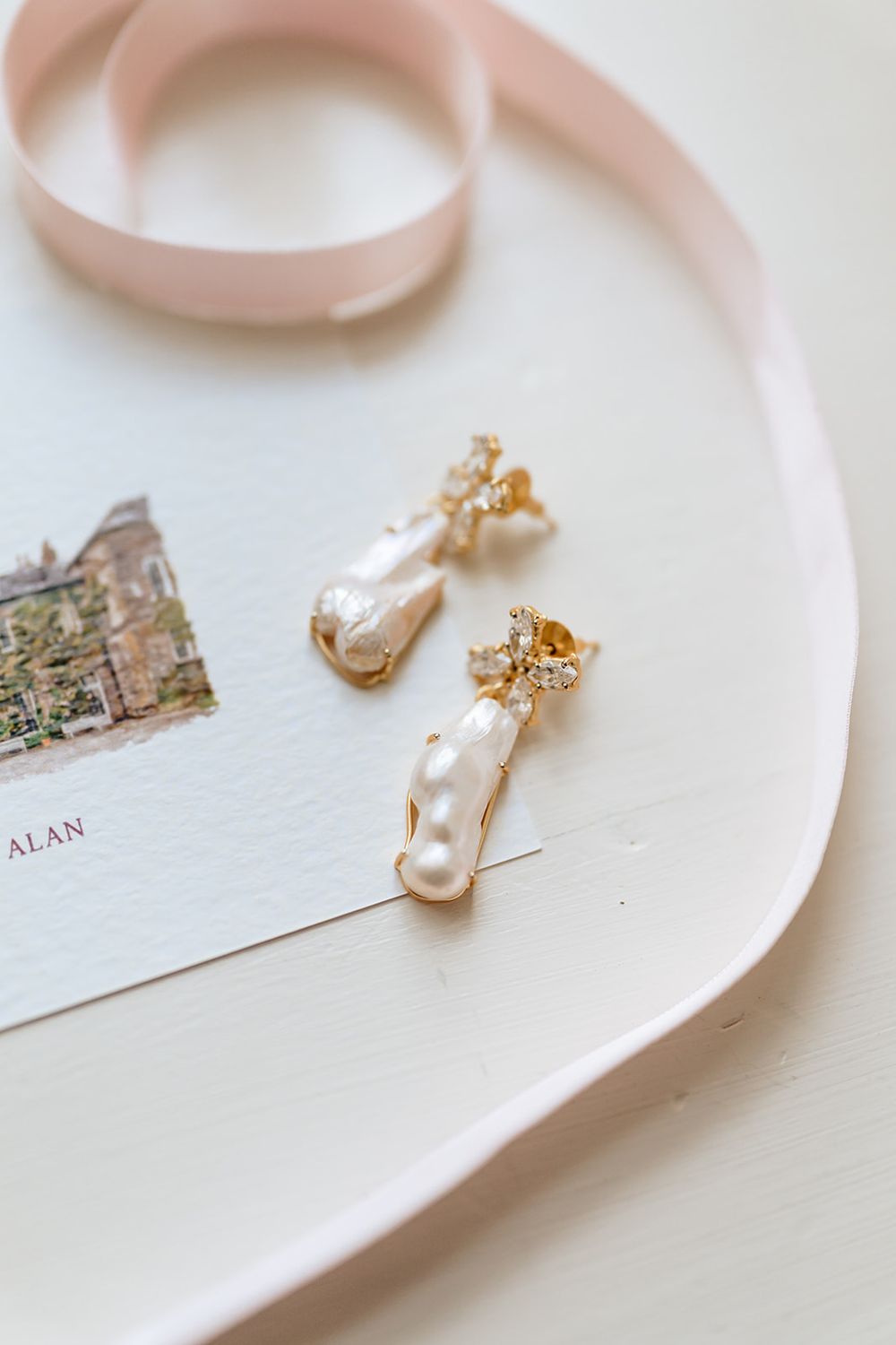 Delicate pearl and gold earrings displayed on white ceramic plates against a light neutral background.