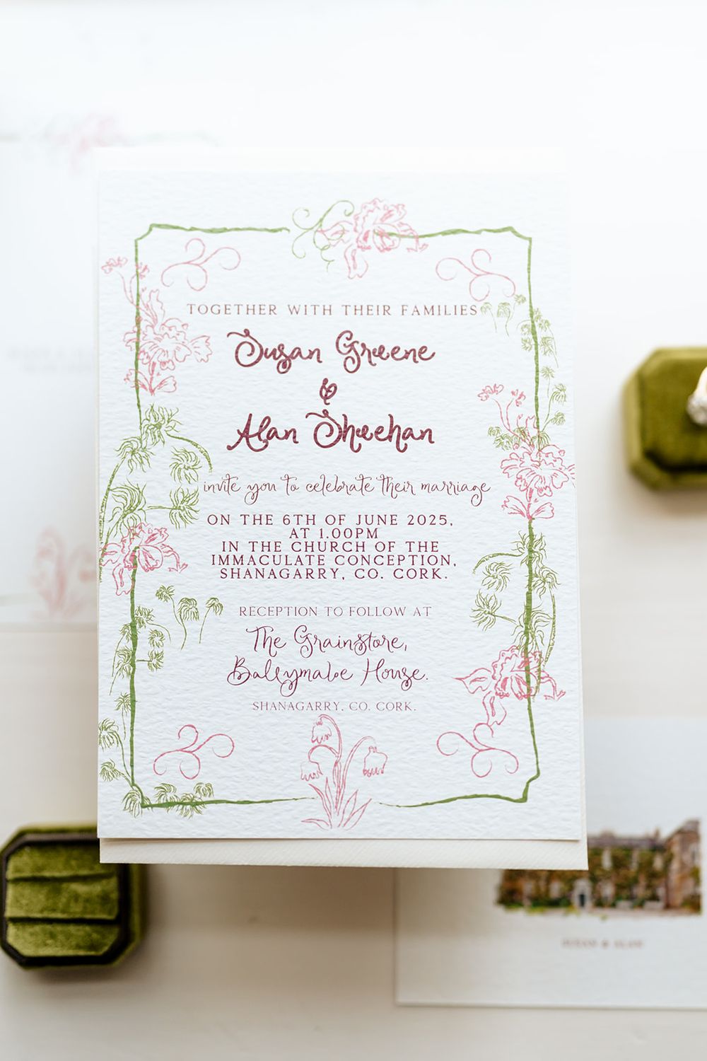 Close-up view of elegant white wedding invitations with delicate green and pink floral calligraphy text designs.