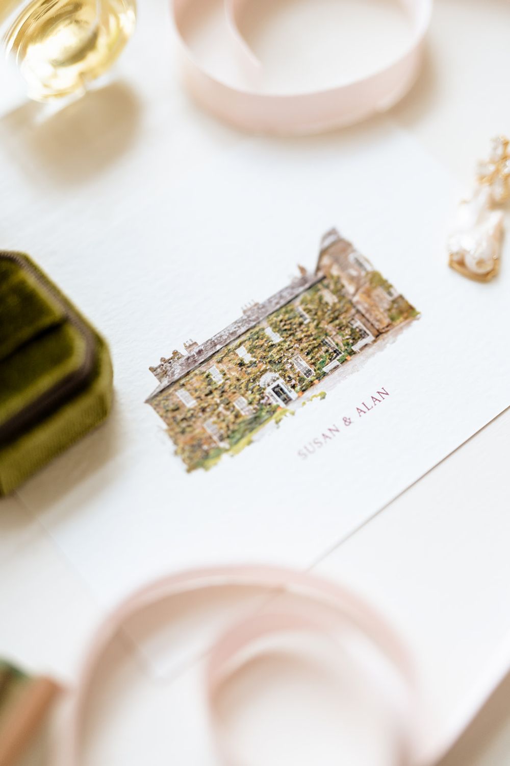 Wedding invitation with delicate watercolor venue illustration surrounded by pink and gold details.