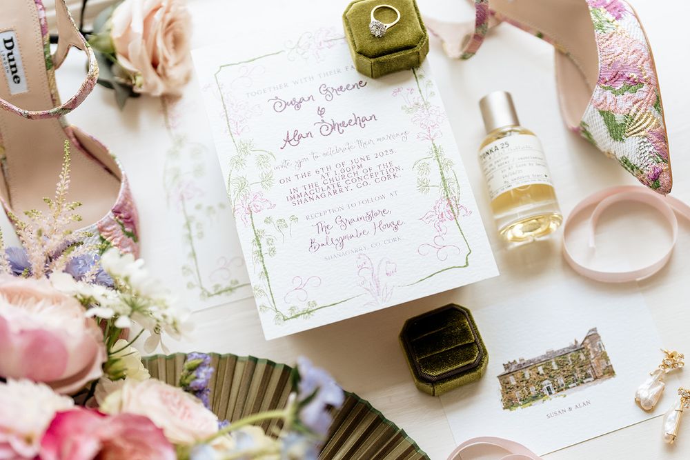 Wedding stationery and decorative items arranged with pink and floral accents on a white surface.