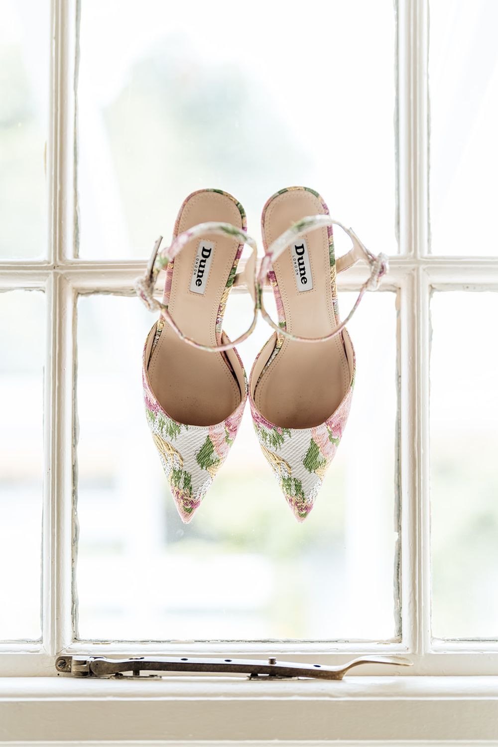 Delicate floral print wedding shoes displayed on a white windowsill in natural light.