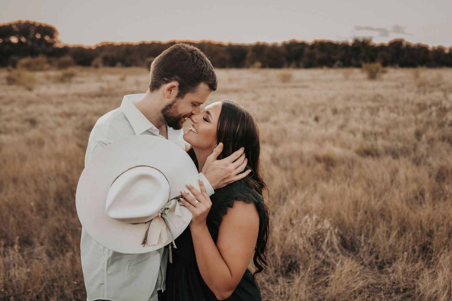 Engagement photos of a sweet couple kissing in a field of golden grass at sunset for their save the date photos