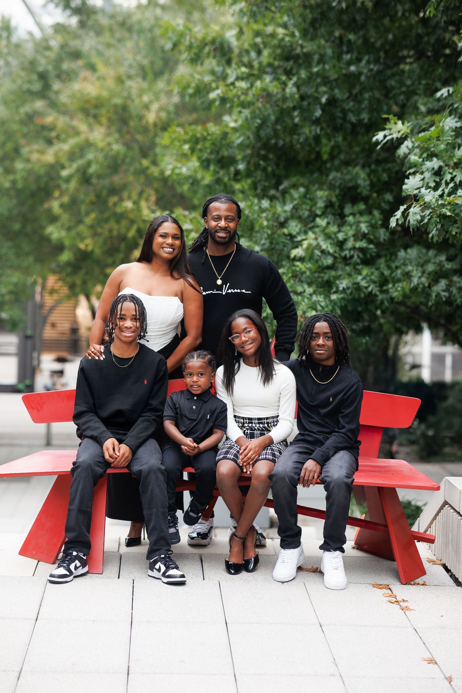 Family dressed in coordinating black and white outfits poses together on red picnic bench for family portraits in Dallas
