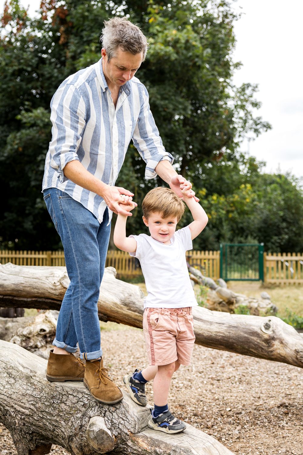 dad holding son's hands while walking on wooden trunk