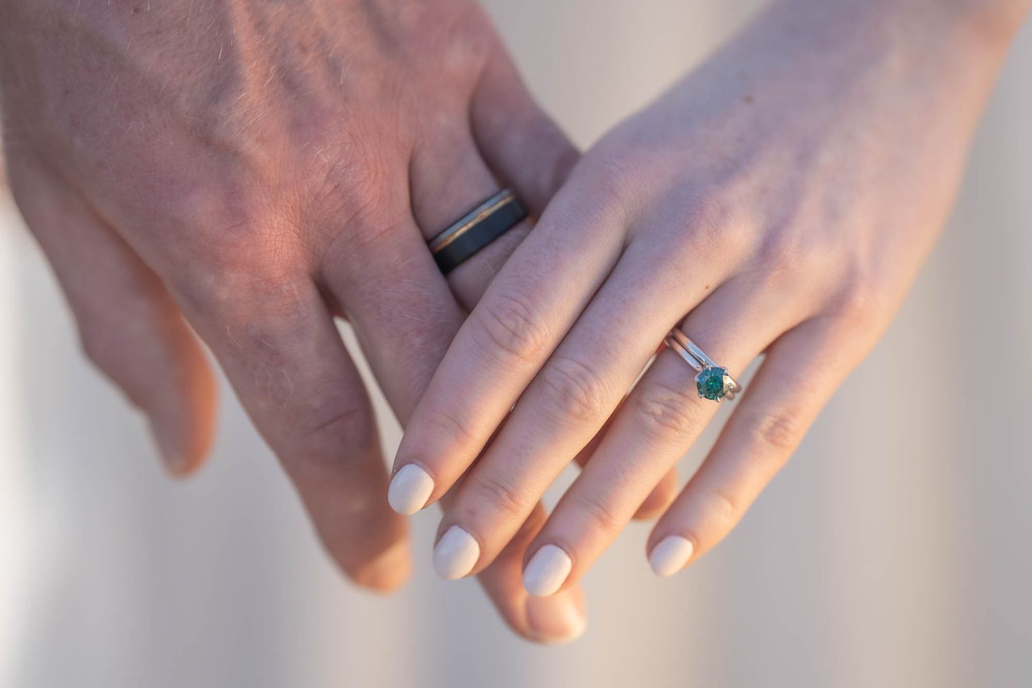 Two hands touch tenderly showing an elegant engagement ring with a blue stone and simple white manicure.