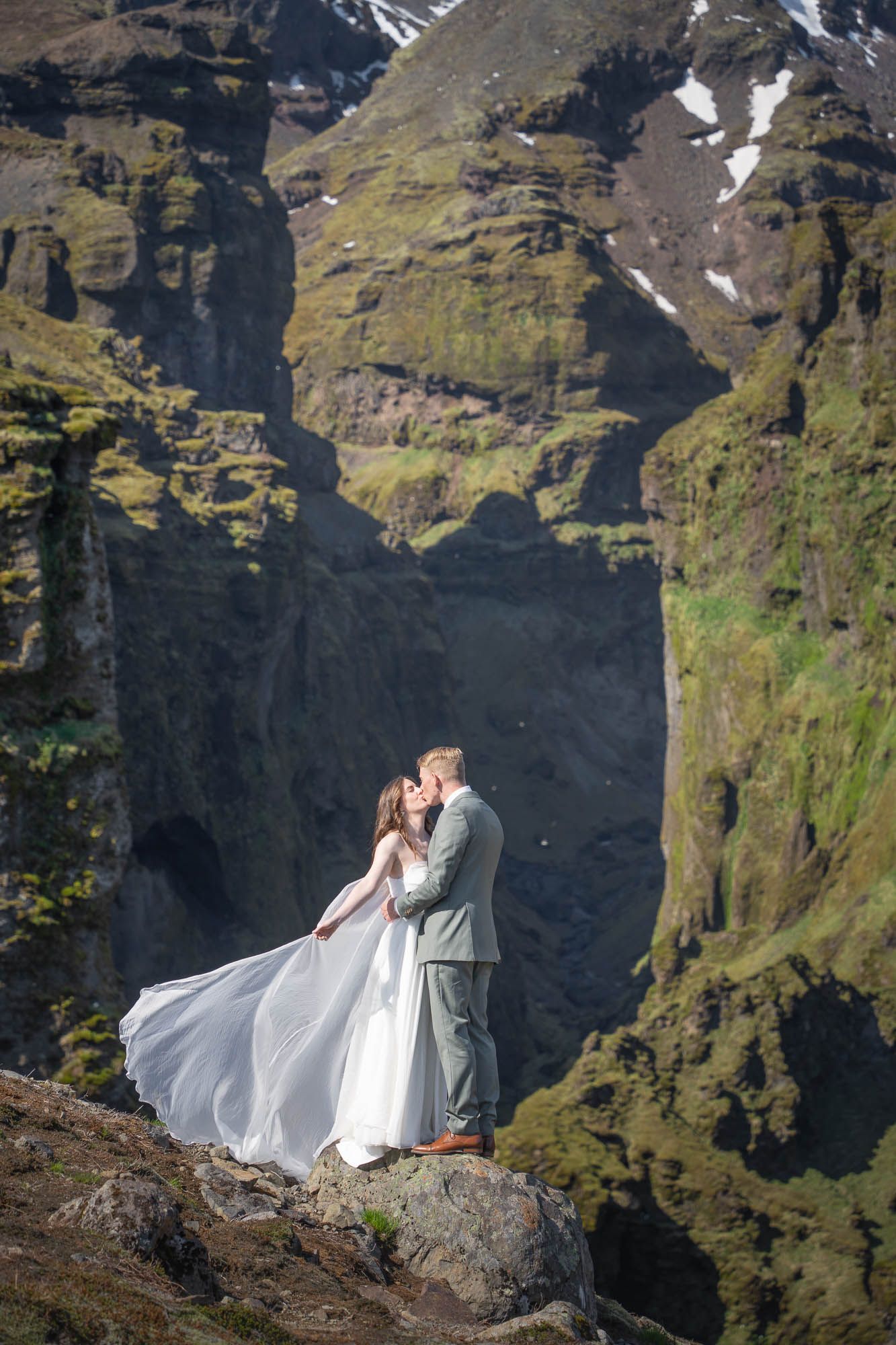 A couple having wedding photos taken against dramatic mountain cliffs in Iceland with a flowing white dress.