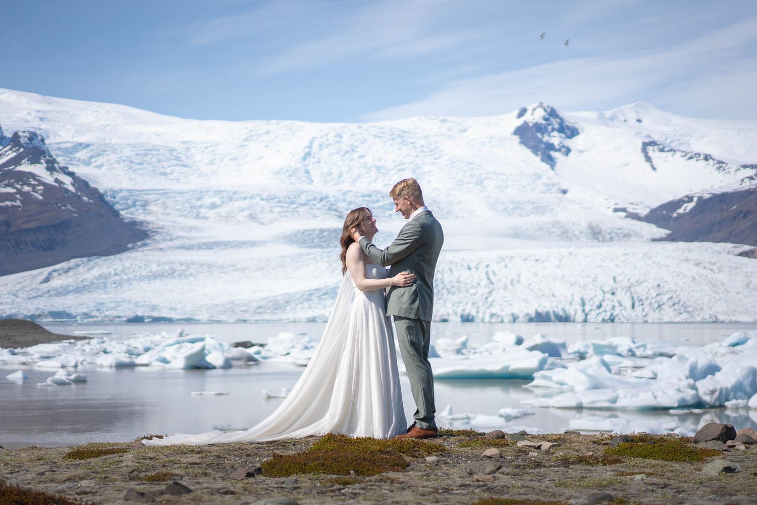Wedding couple embracing in front of massive glacier and icy lake landscape.
