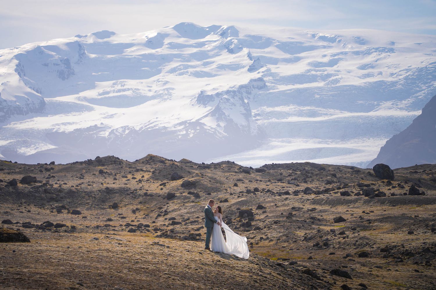 Couple standing together against snowy mountain peaks in a dramatic Icelandic landscape.