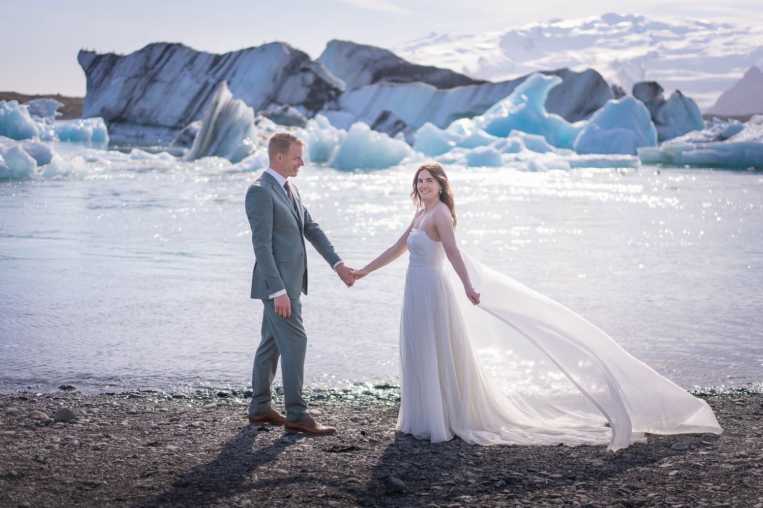 A wedding couple poses on a beach with stunning blue icebergs and glaciers in the background.