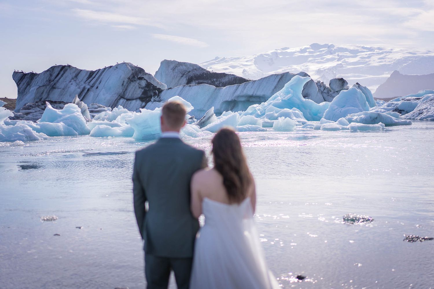 Couple admiring massive blue icebergs floating in a glacial lagoon during sunset.