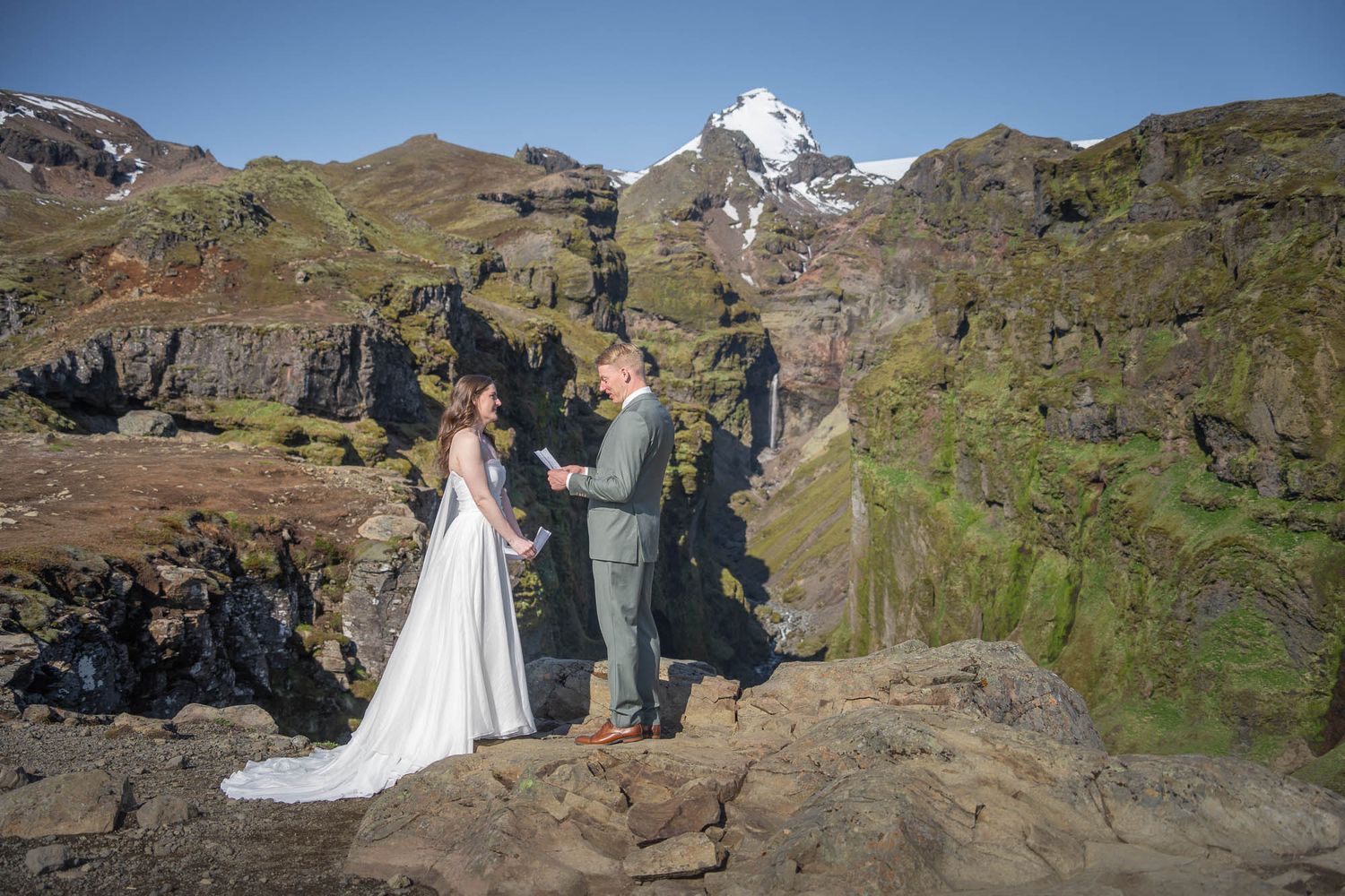 Wedding ceremony taking place on a dramatic cliff edge with mountain peaks in the background.