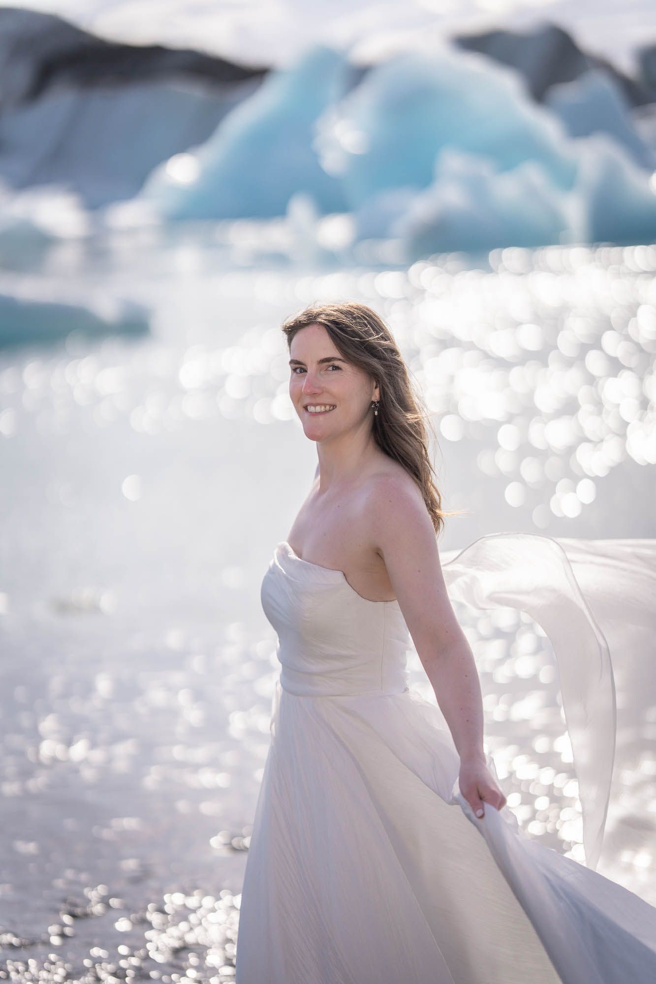 A bride in white dress twirling joyfully against a sparkling glacial backdrop.
