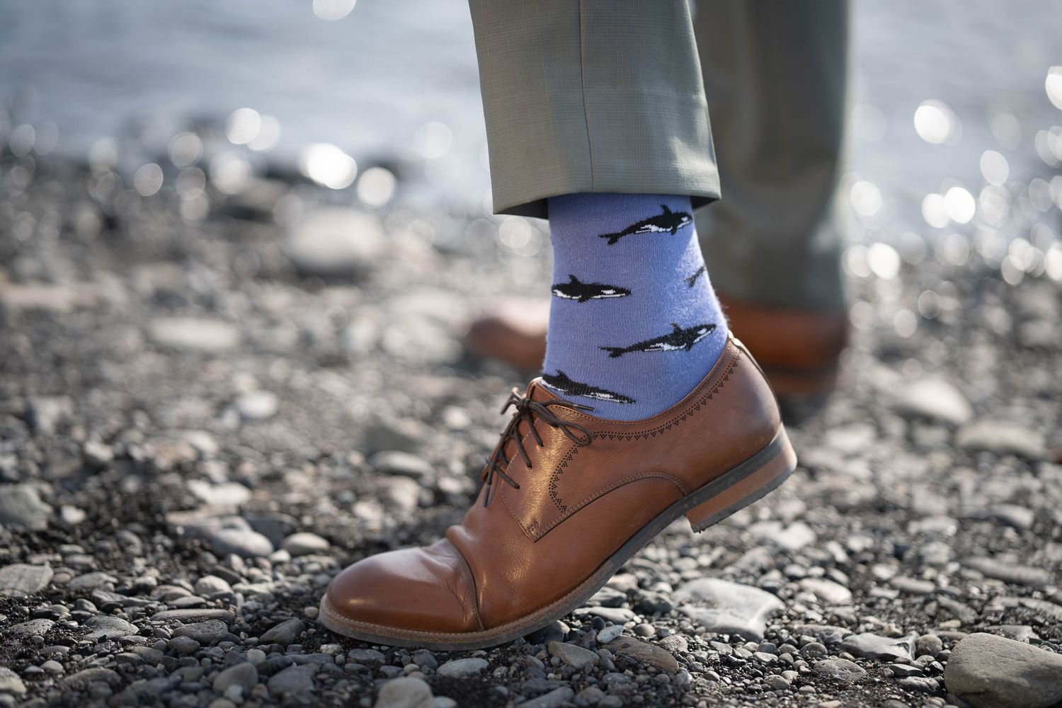 Brown leather dress shoe and playful sock with bat pattern shown against rocky ground.