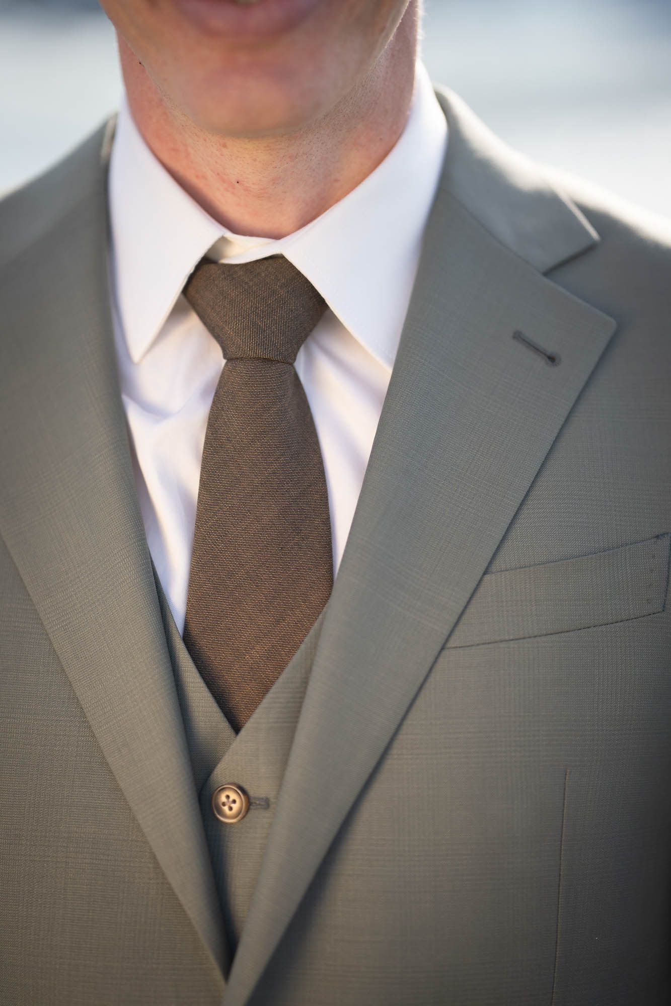 Close-up detail of a gray three-piece suit with brown tie and crisp white collar.