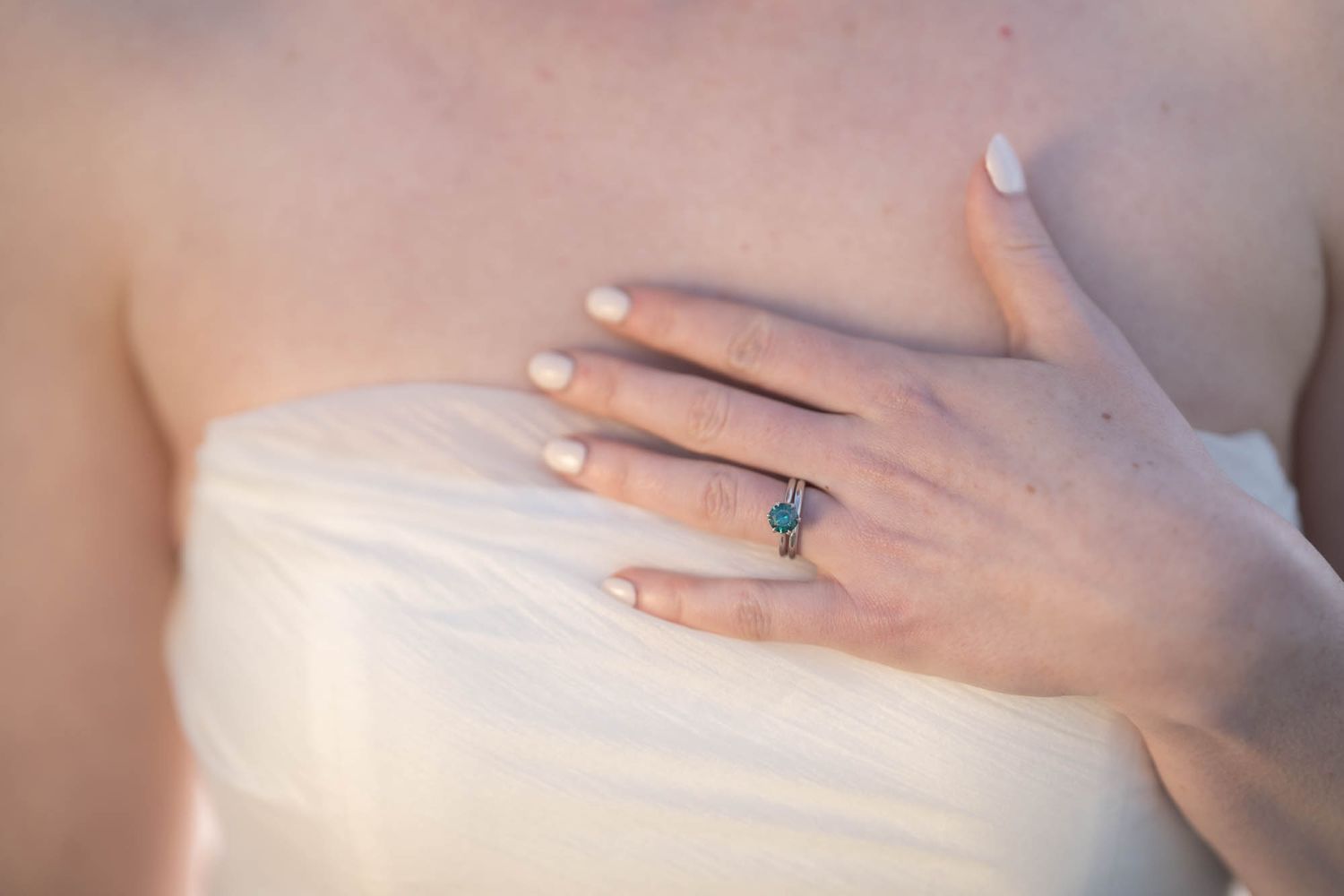 Elegant engagement ring on woman's hand resting against white fabric.