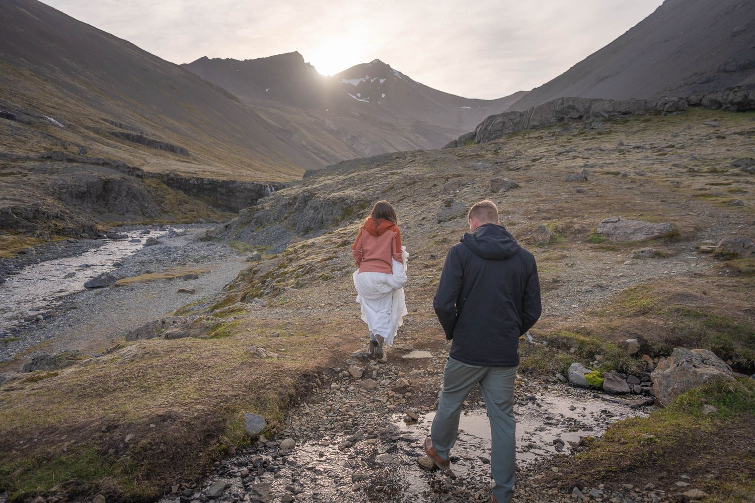 Two people walking along a mountain trail at sunset with dramatic valley views.