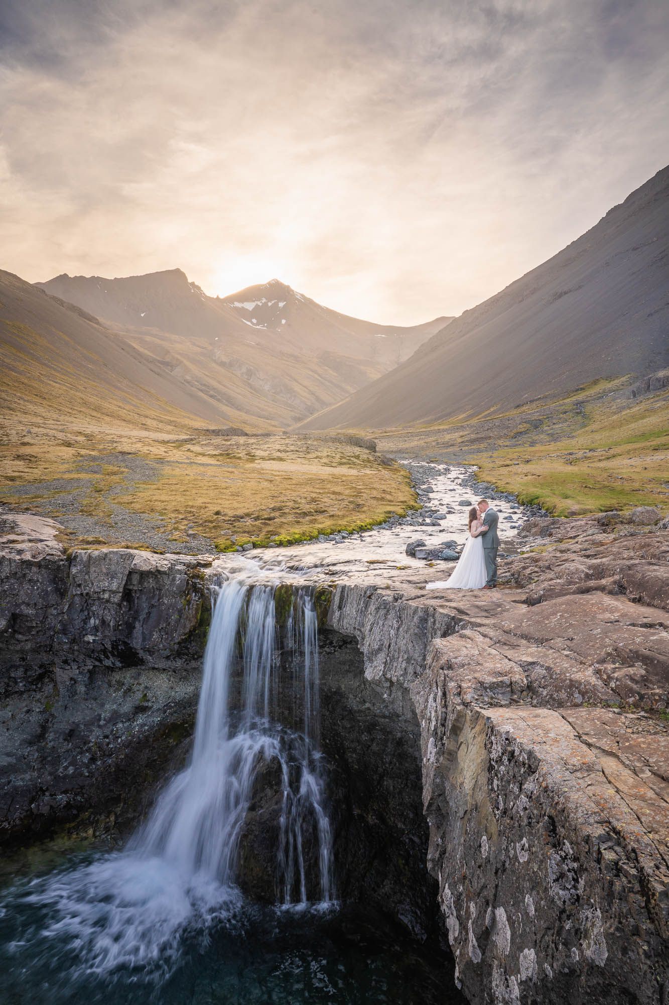 Majestic waterfall cascading over rocky cliffs in a mountainous valley during sunset.
