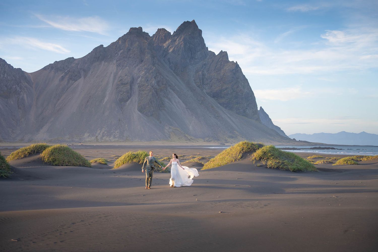 Two figures walk along black sand beach with dramatic Vestrahorn mountain peak rising in background in Iceland.