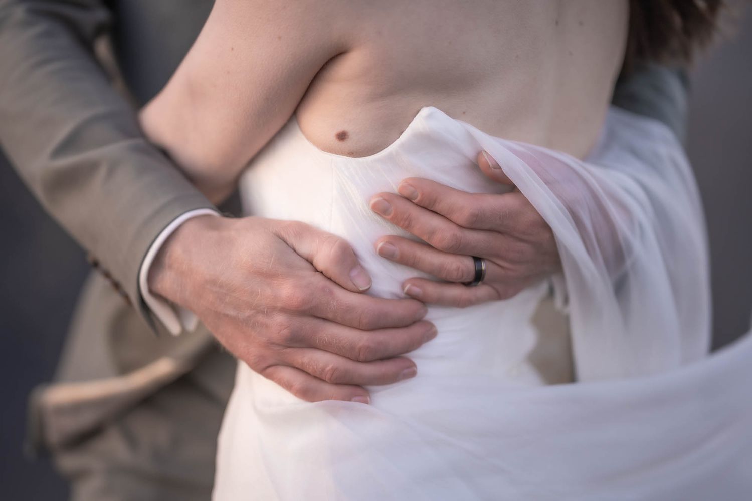 Intimate close-up of hands embracing around a white dress fabric with soft romantic lighting.