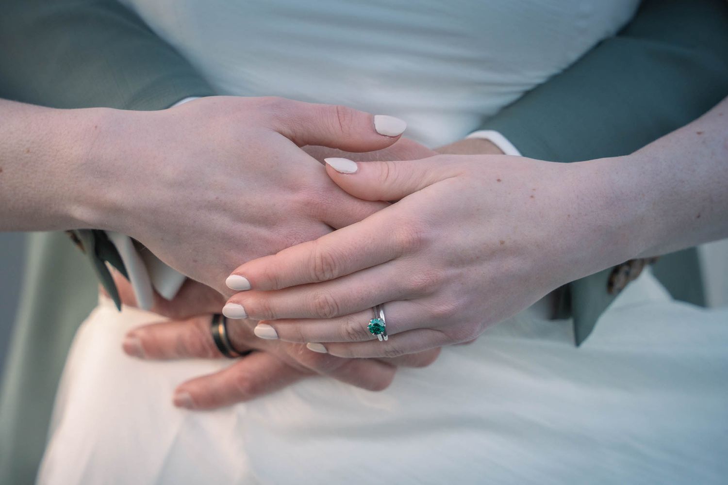 Close-up view of hands with wedding rings and white lace dress fabric.