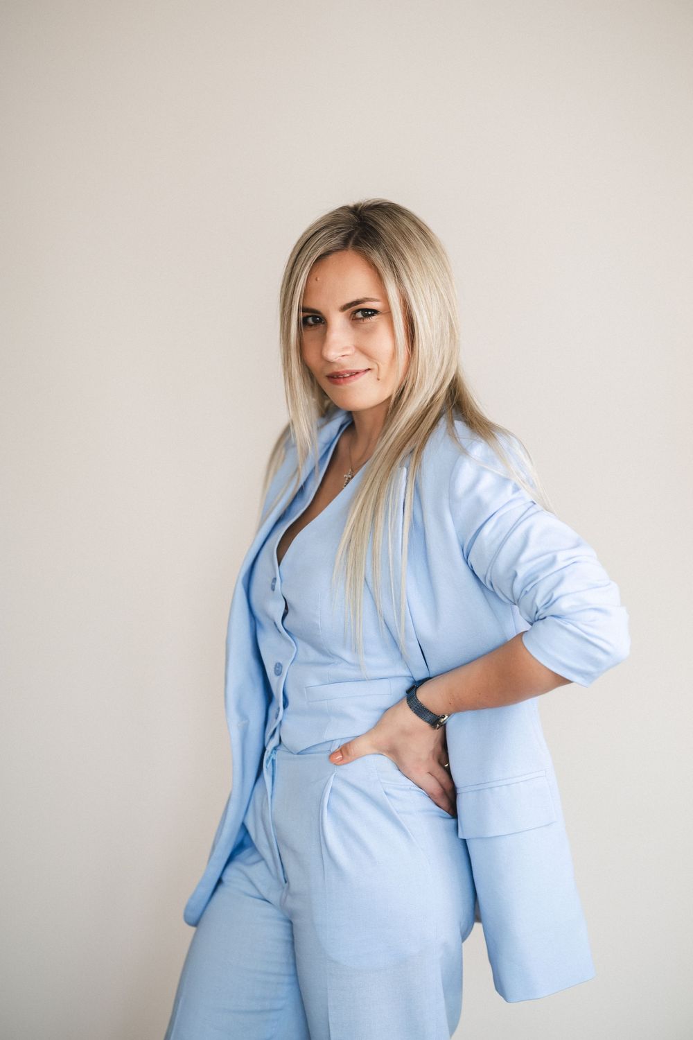 Stylish business professional in powder blue pantsuit poses against neutral backdrop.