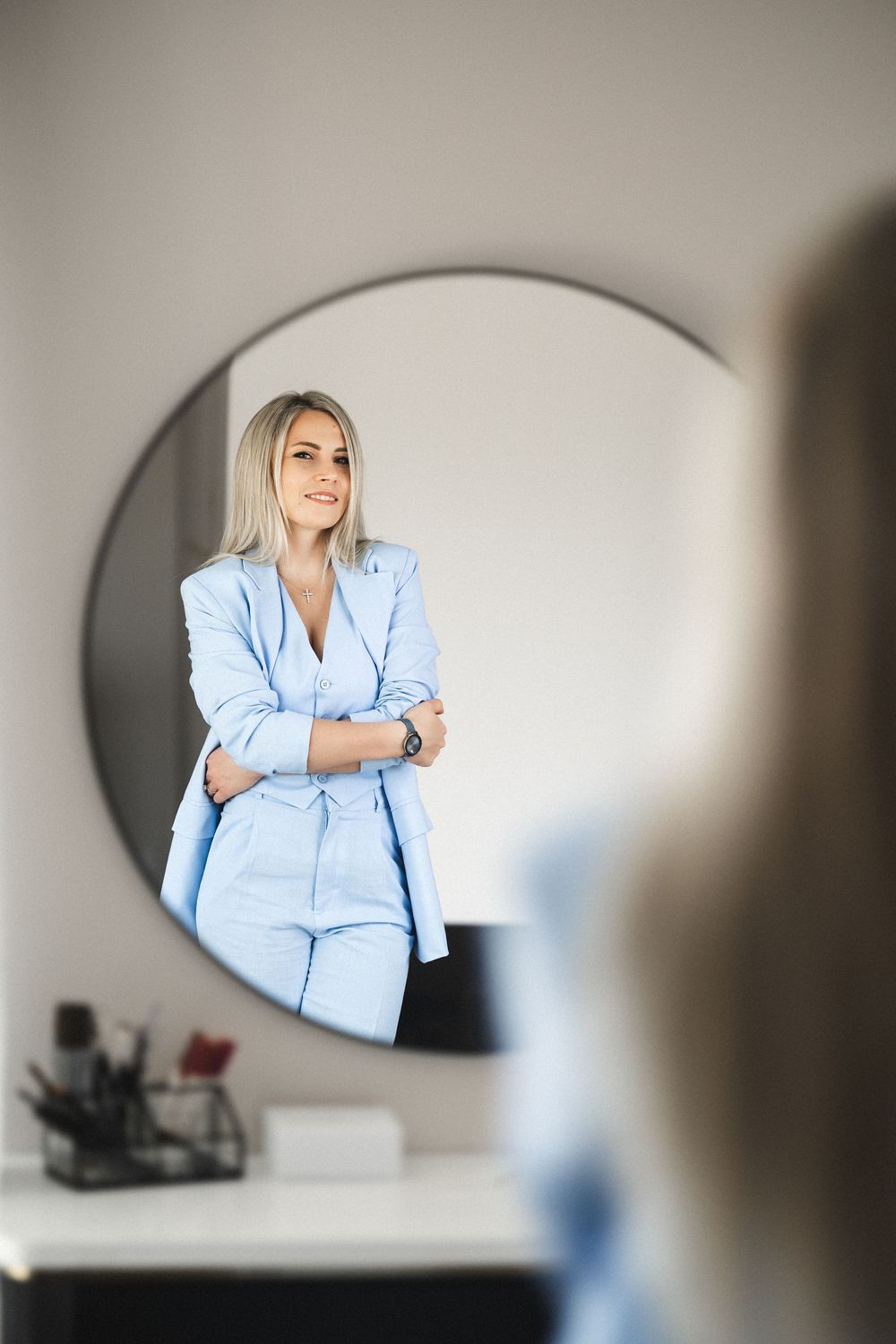 Reflection in round mirror shows professional wearing light blue suit against neutral wall.