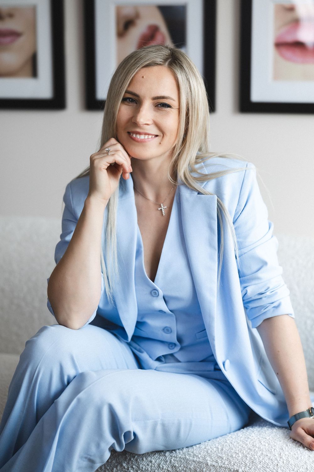 Professional seated on couch in powder blue suit with framed art in background.