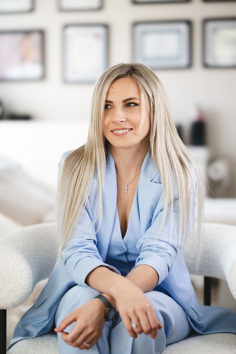 Business professional in light blue suit seated casually on grey couch.