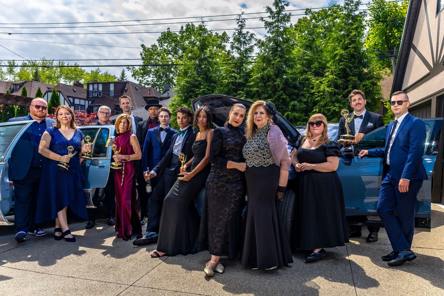 An editorial vogue-style group portrait of several Emmy award winners posing together with their cars