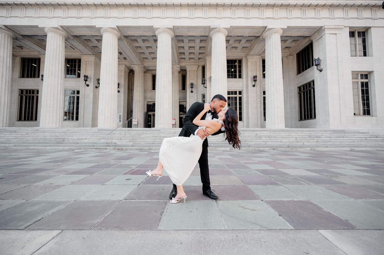 A couple dances in formal attire on a grand marble porch with white columns of a stately building during a special occasion.