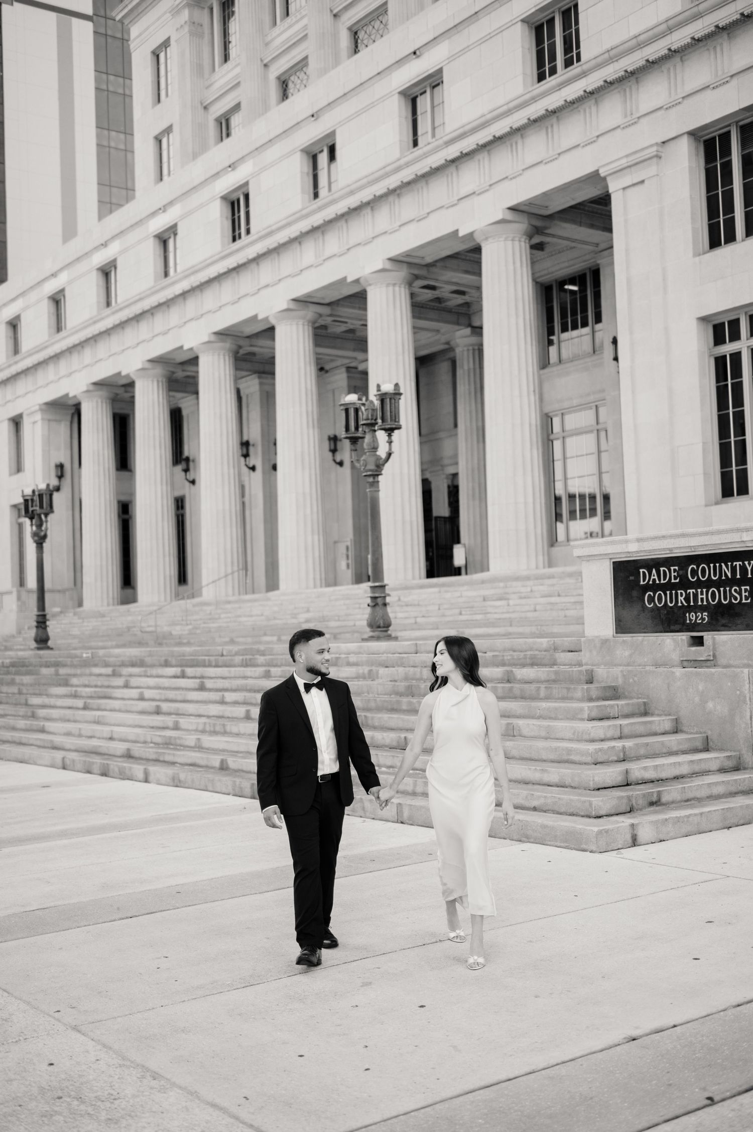 Black and white photo of a couple in formal attire walking outside the Dade County Courthouse with its grand columns.