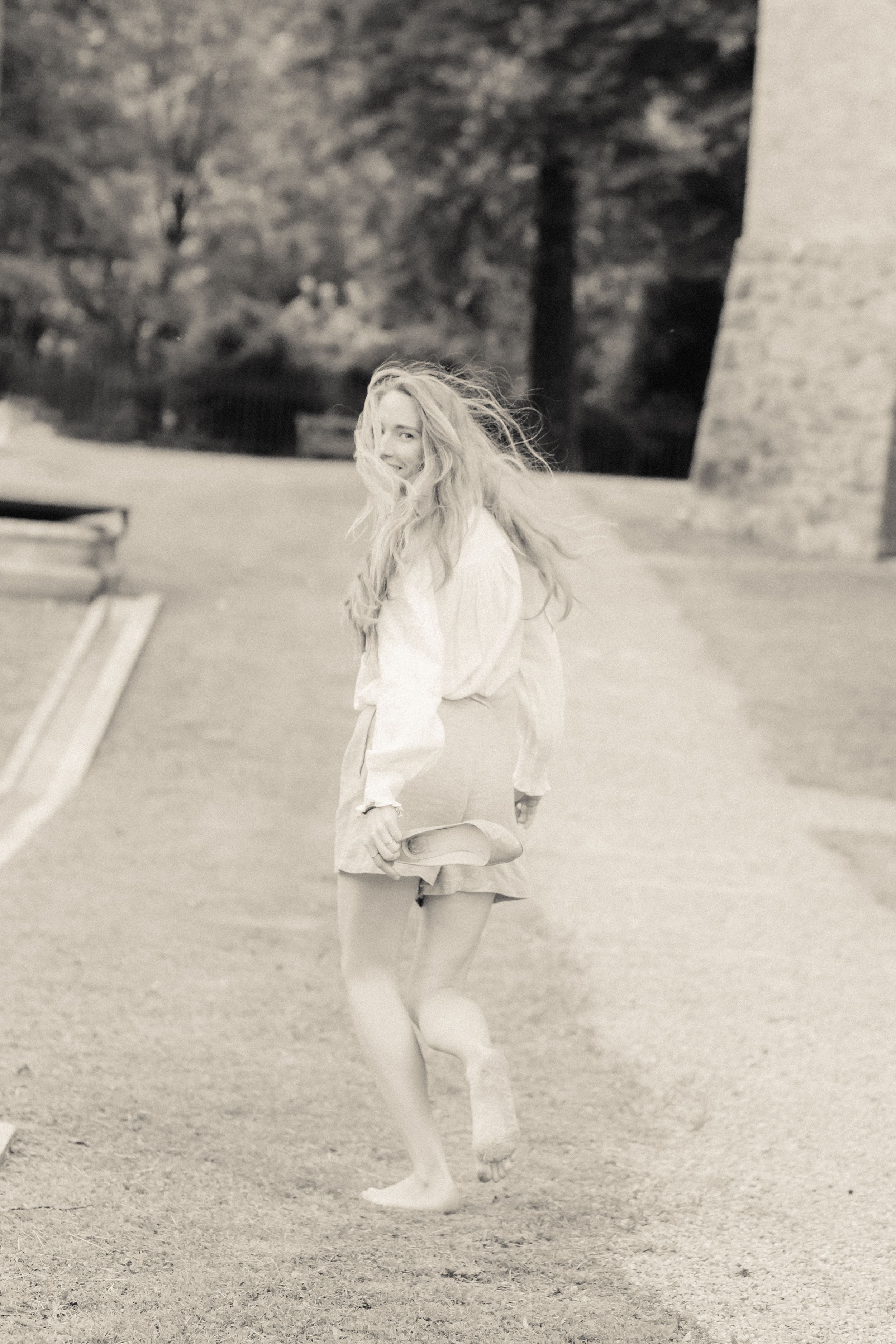 A dreamy black and white photo shows a person with flowing hair twirling on a path in a light summer dress.