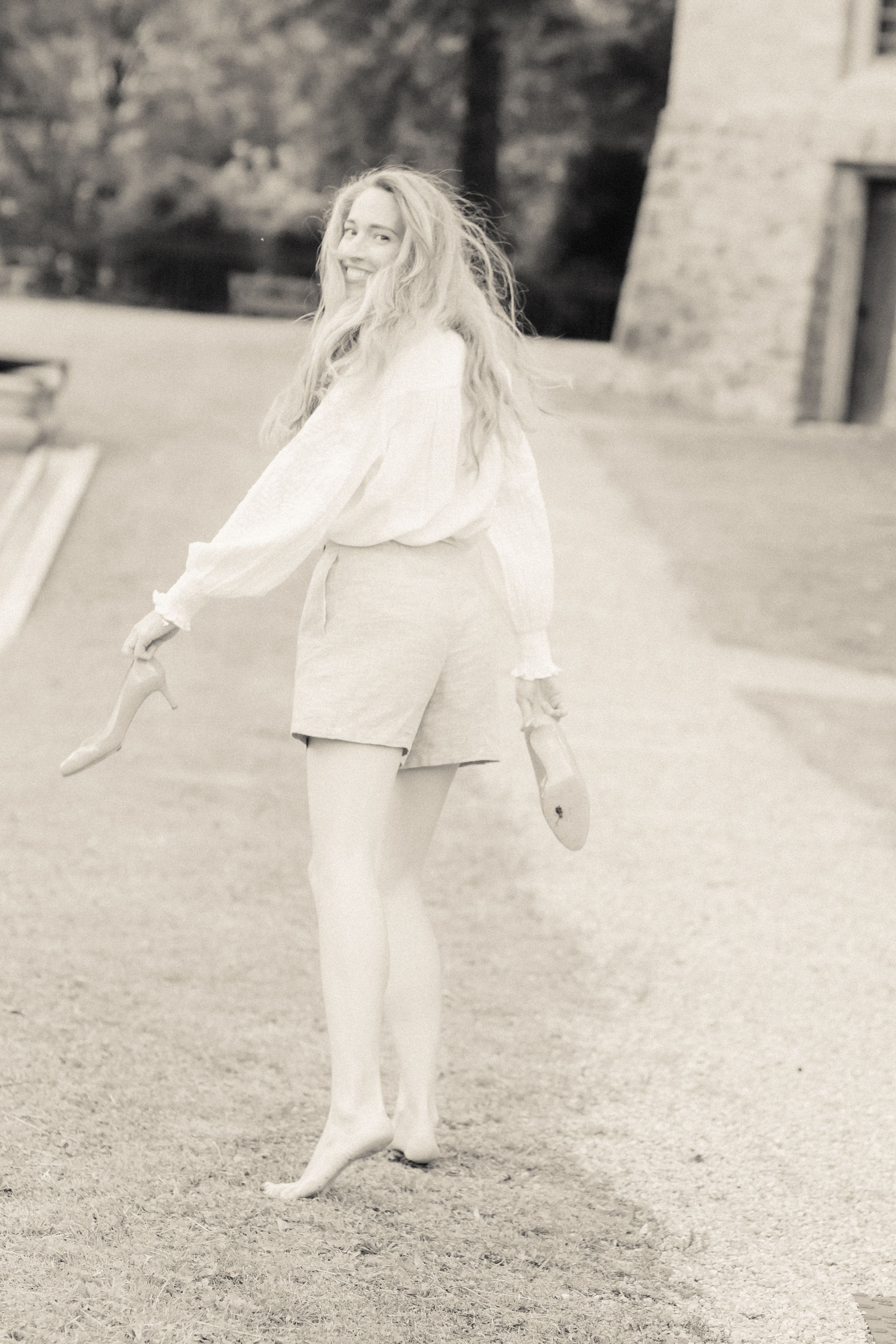 Black and white vintage-style portrait of a person in casual white attire twirling outdoors with long flowing hair.