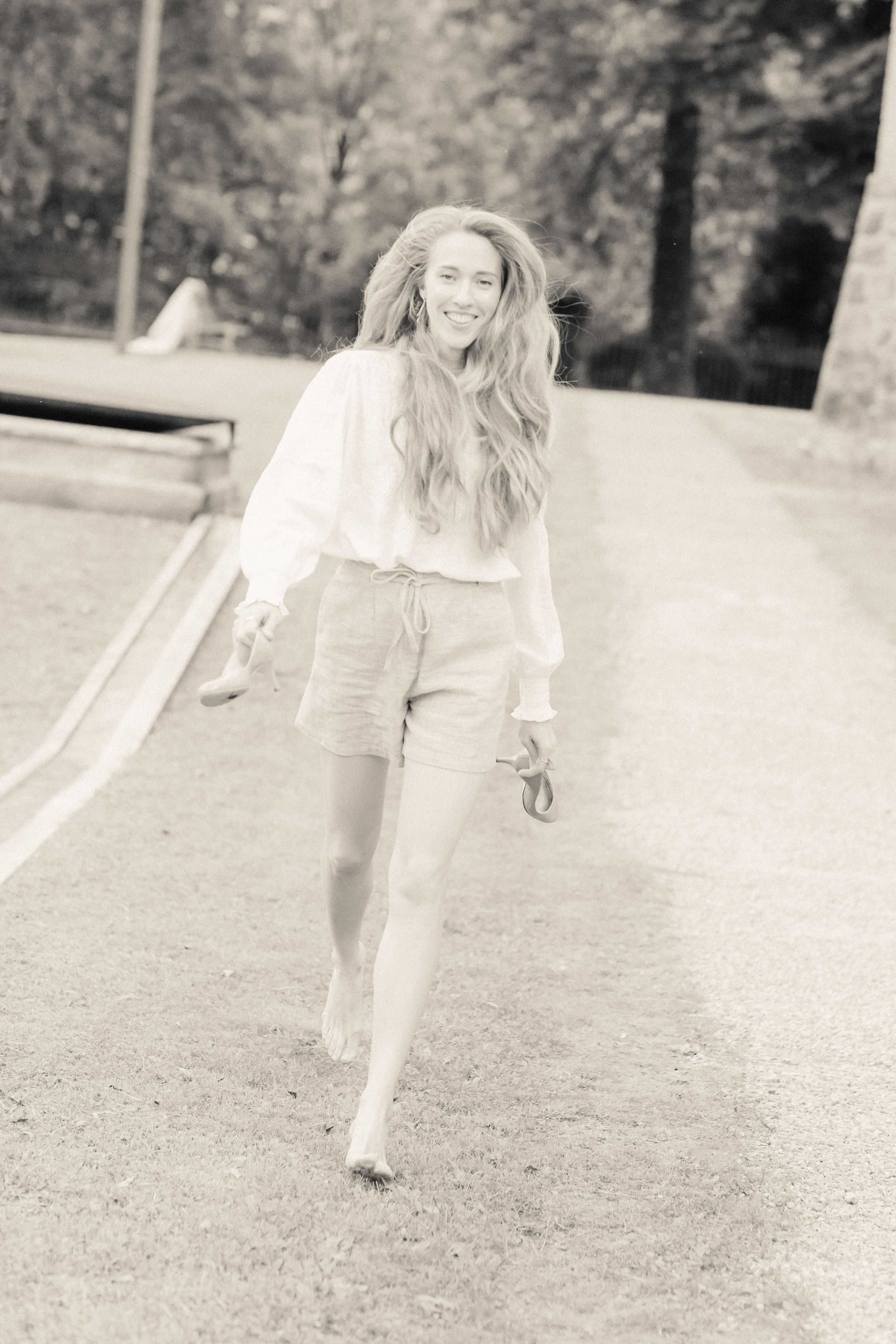 Black and white photo of someone running joyfully on a path wearing shorts and a light top.