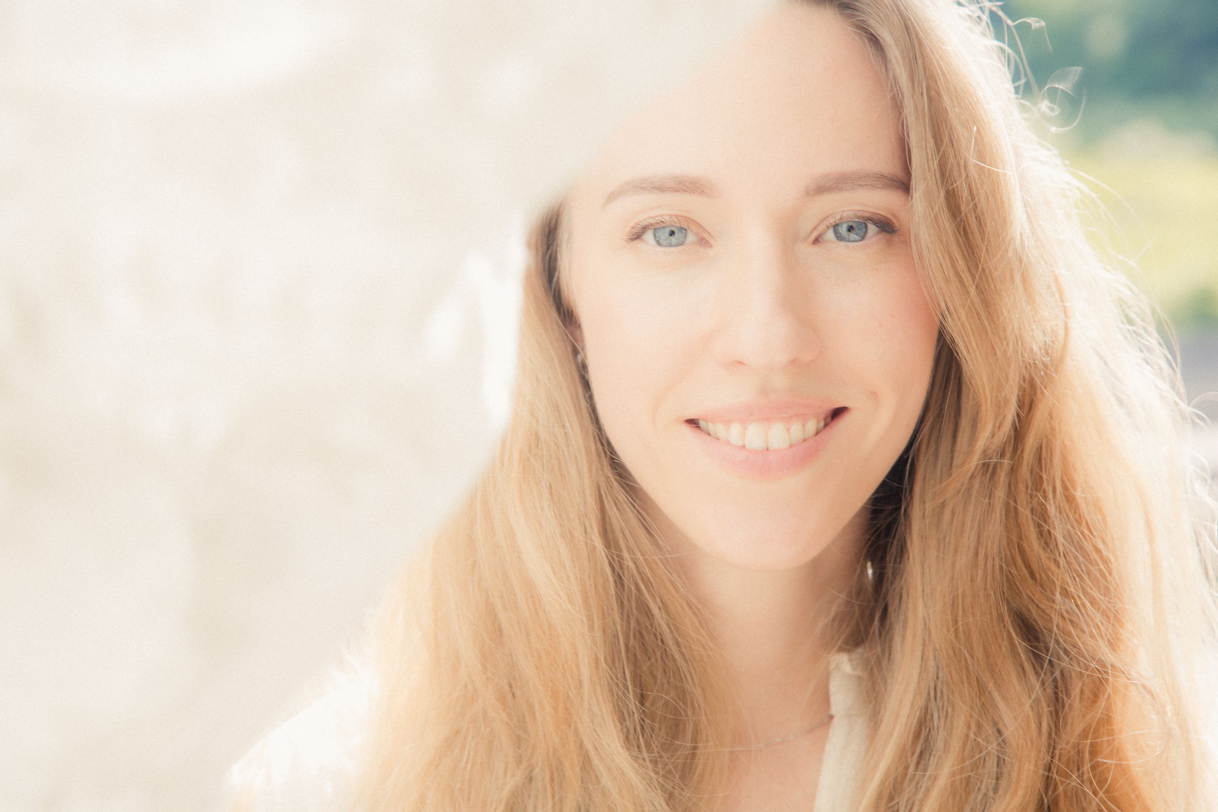 Soft sunlit portrait with natural makeup and flowing blonde hair against a bright background.